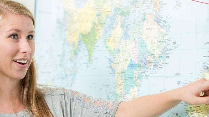 Female student points at wall-sized international map.