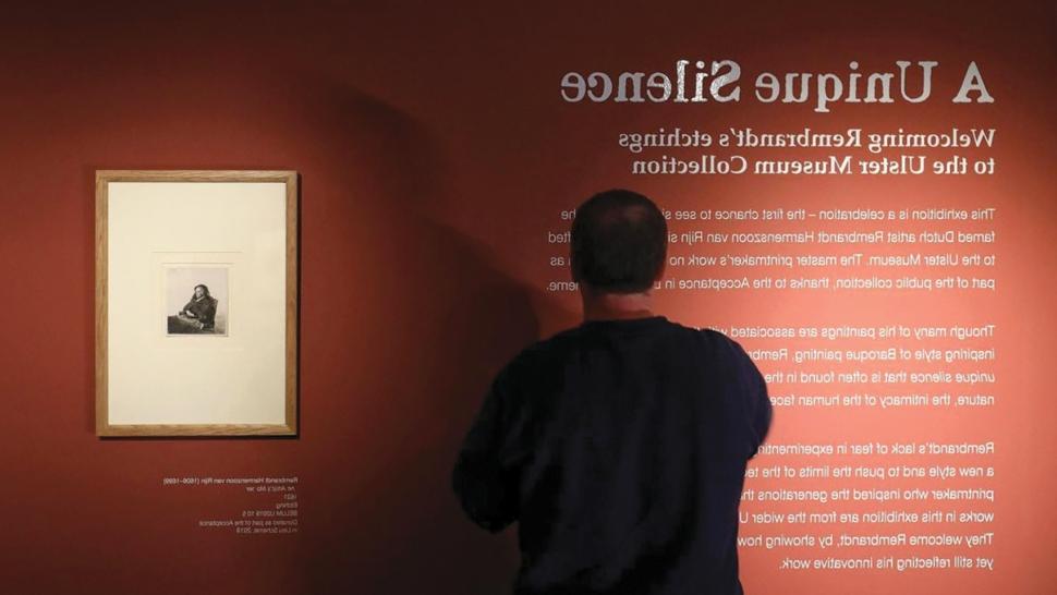 a man reads a description of the "Unique Silence" exhibit, written on a large burnt-orange wall